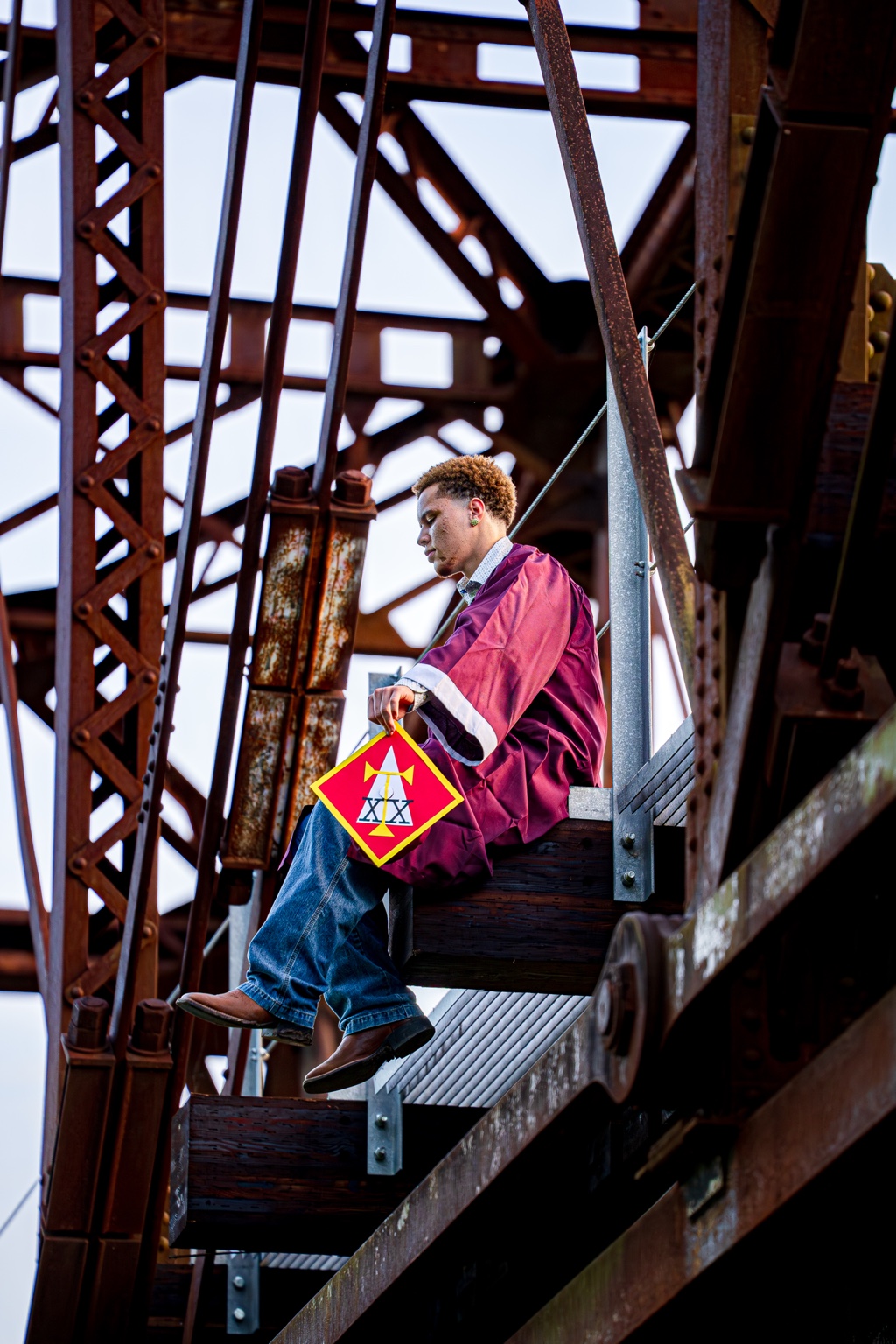 Graduate in cap and gown seated on a steel bridge